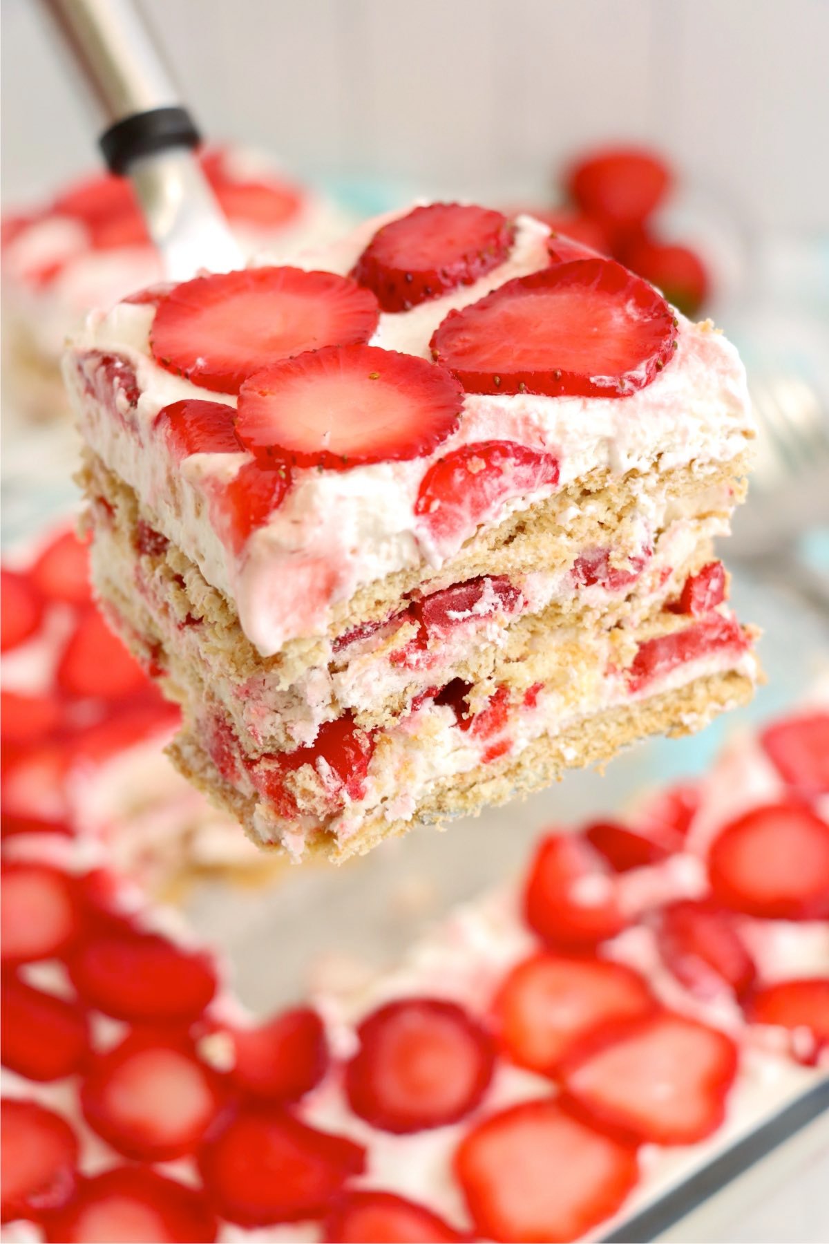 Slice of strawberry icebox cake lifted from the pan showing layers of cream, strawberries, and graham crackers.