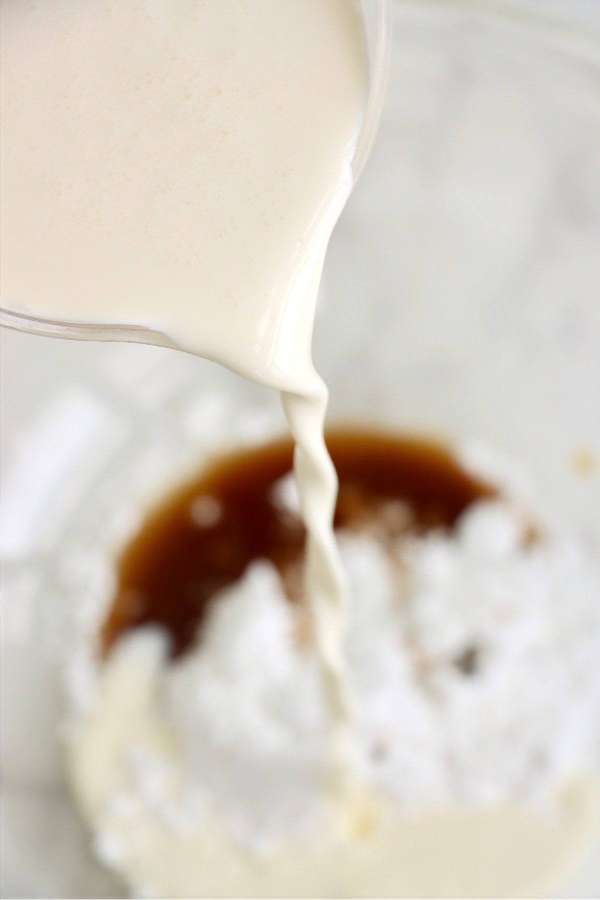 Pouring cream into a mixing bowl with vanilla and powdered sugar.