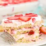 Partially eaten slice of strawberry icebox cake on a plate with a fork and a halved strawberry.