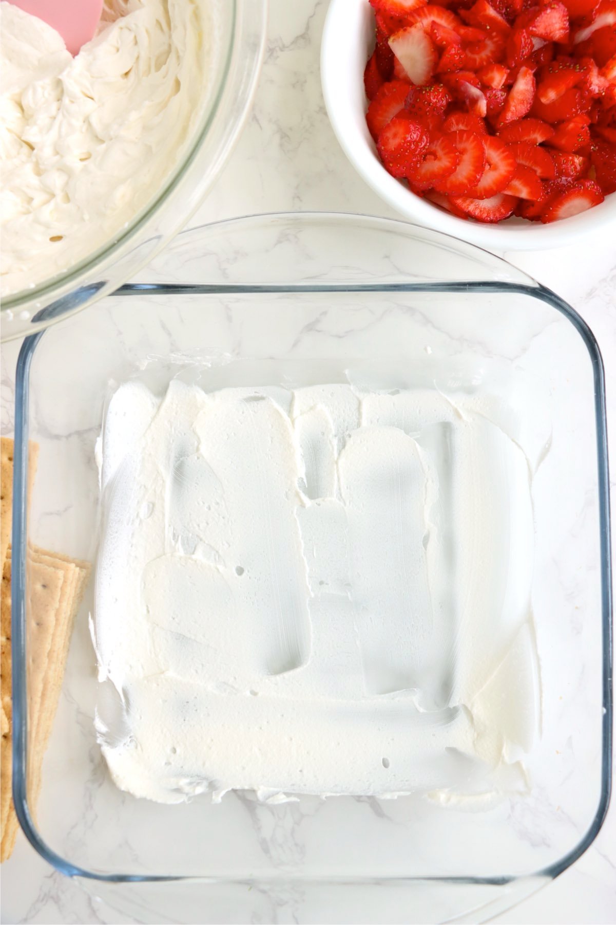 Whipped cream spread in the bottom of a square glass baking dish.