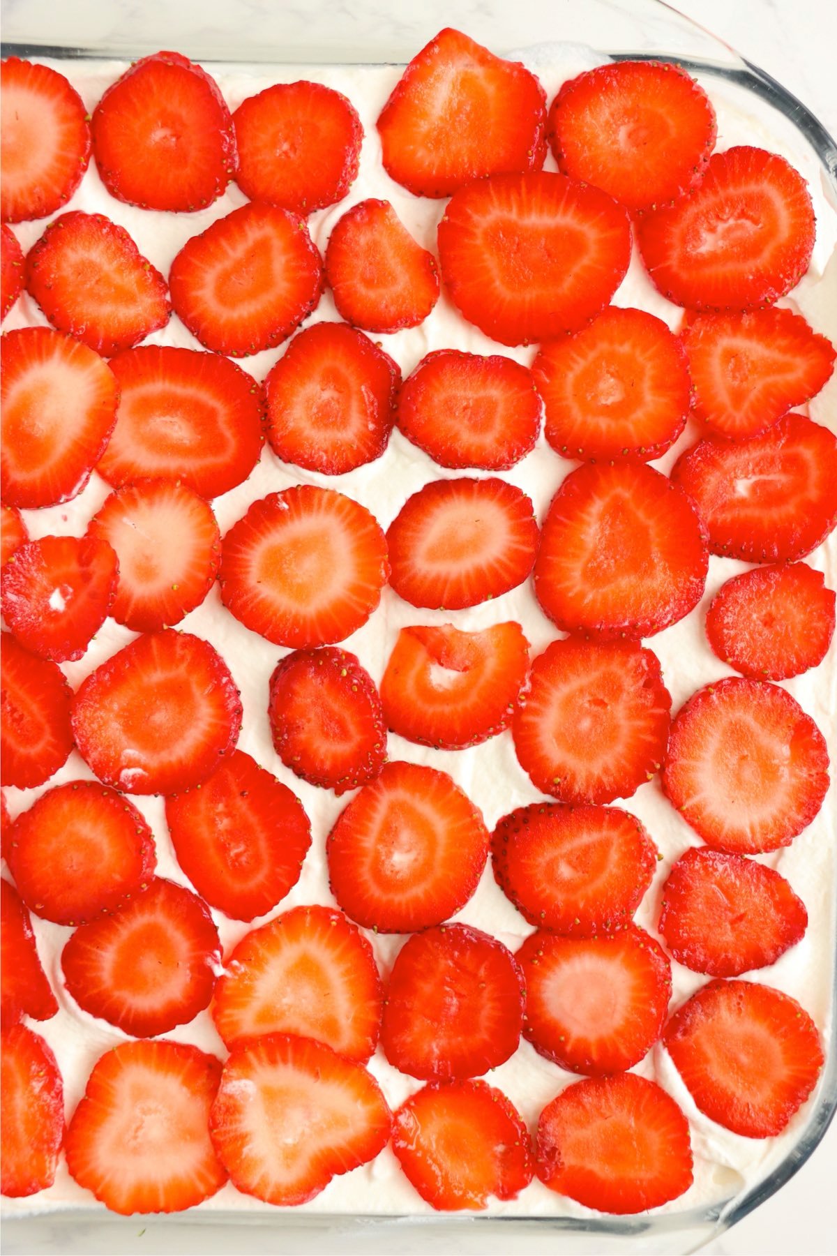 Even layer of sliced strawberries covering whipped cream.