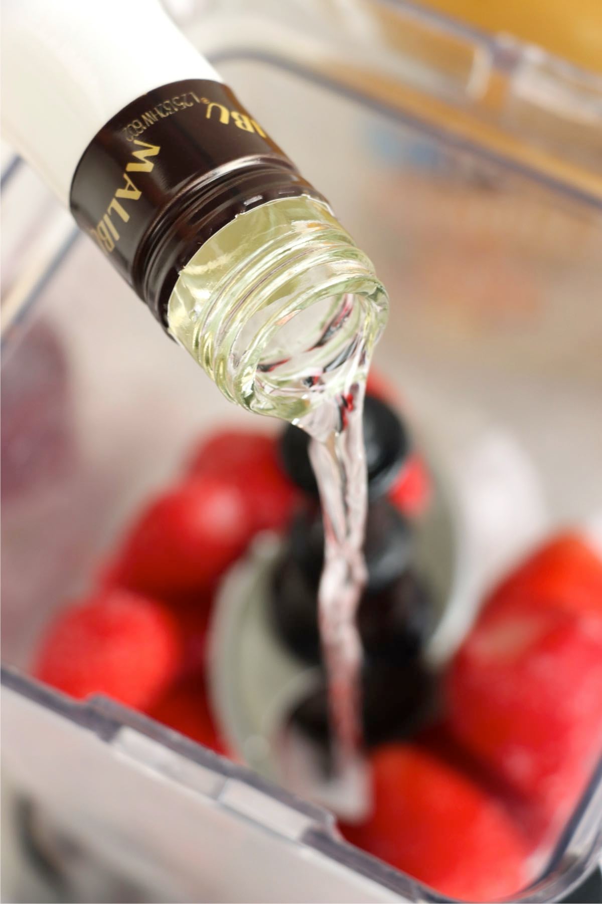 Malibu rum being poured over frozen strawberries in a blender.