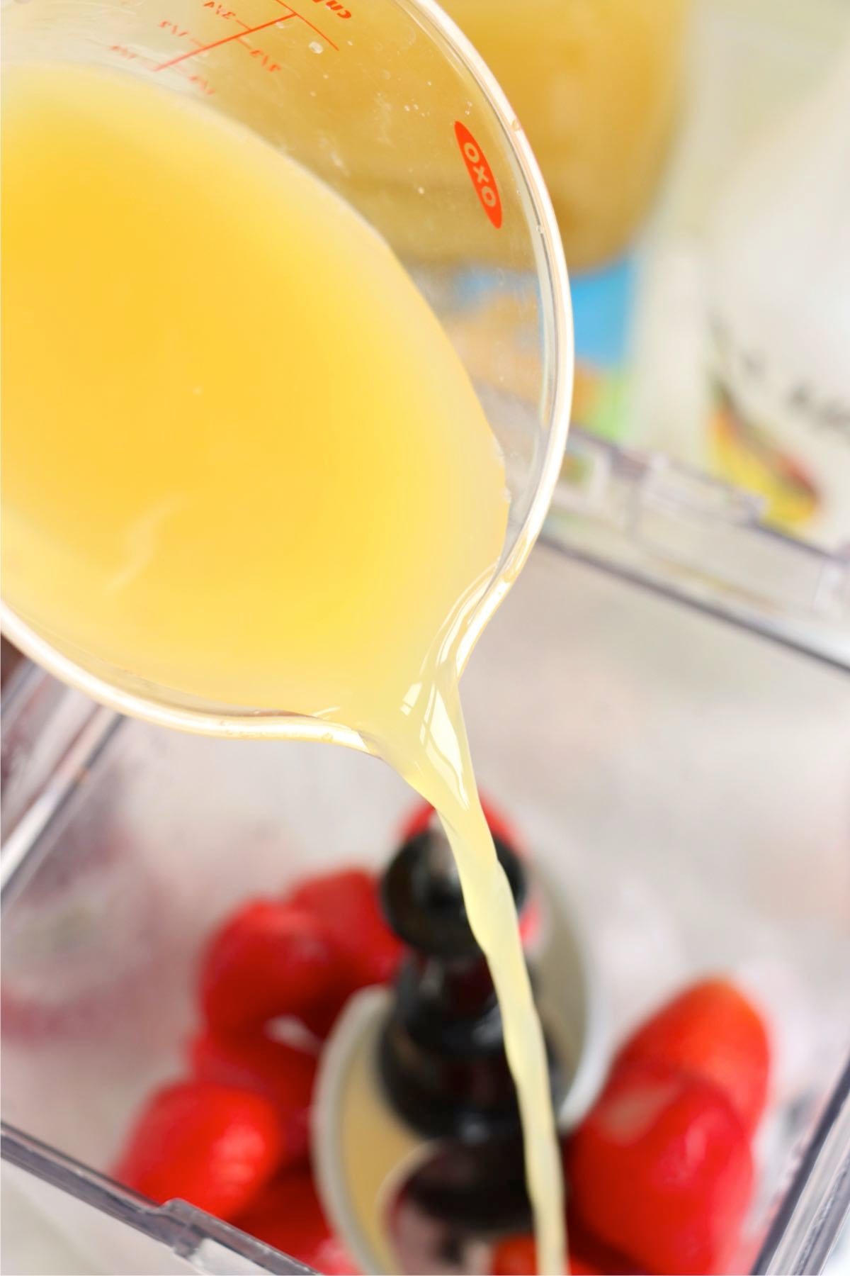 Pineapple juice being poured into a blender with strawberries.