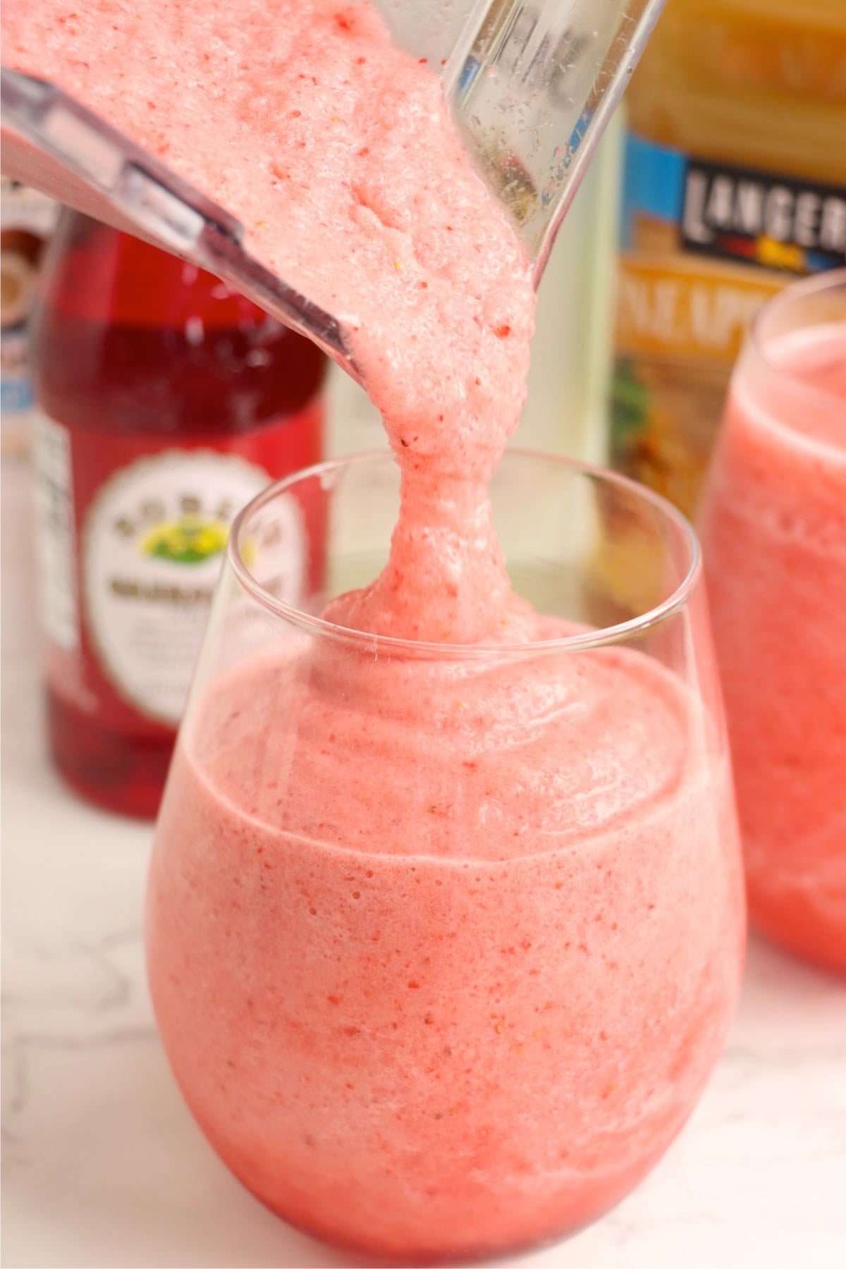 A pink blended drink being poured into a glass.