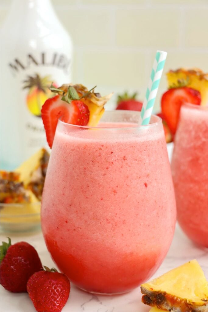 A pink tropical drink in a glass garnished with pineapple and strawberry.