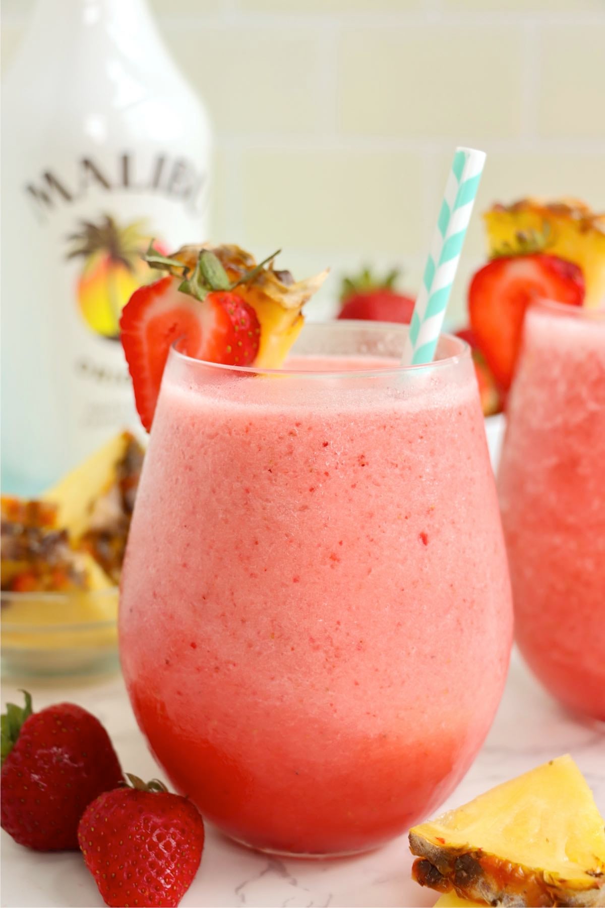 A pink tropical drink in a glass garnished with pineapple and strawberry.