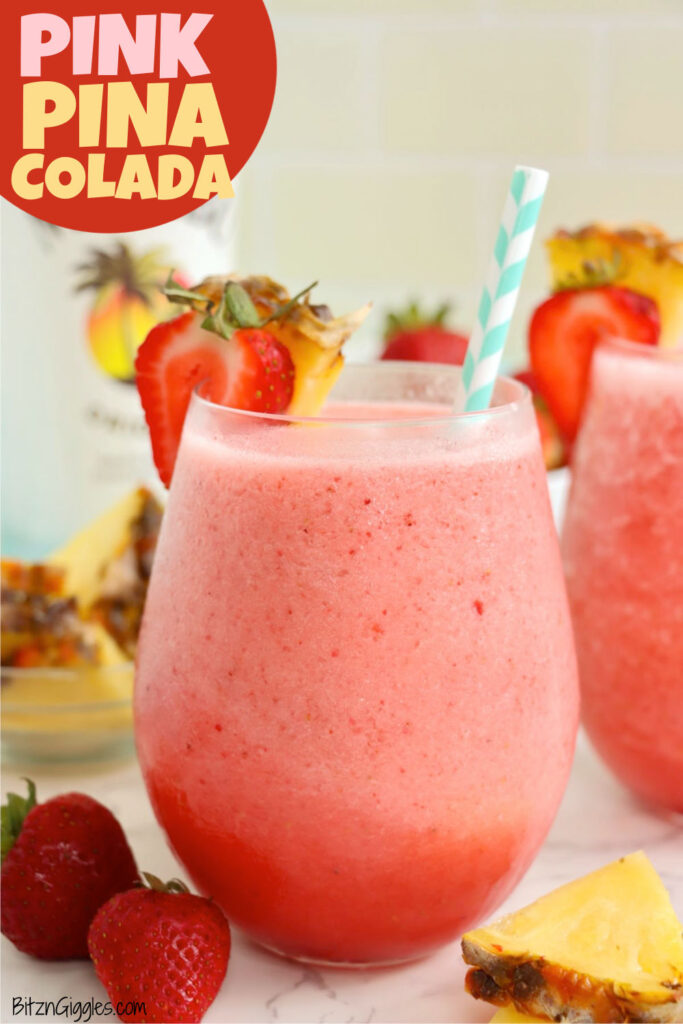 A glass of pink blended drink with a striped straw and fruit garnish, with fresh strawberries and pineapple on the side.