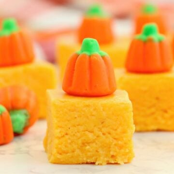 Pumpkin fudge squares topped with candy pumpkins arranged on a white surface.