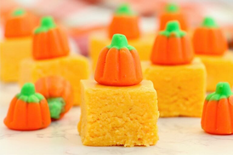 Pumpkin fudge squares topped with candy pumpkins arranged on a white surface.