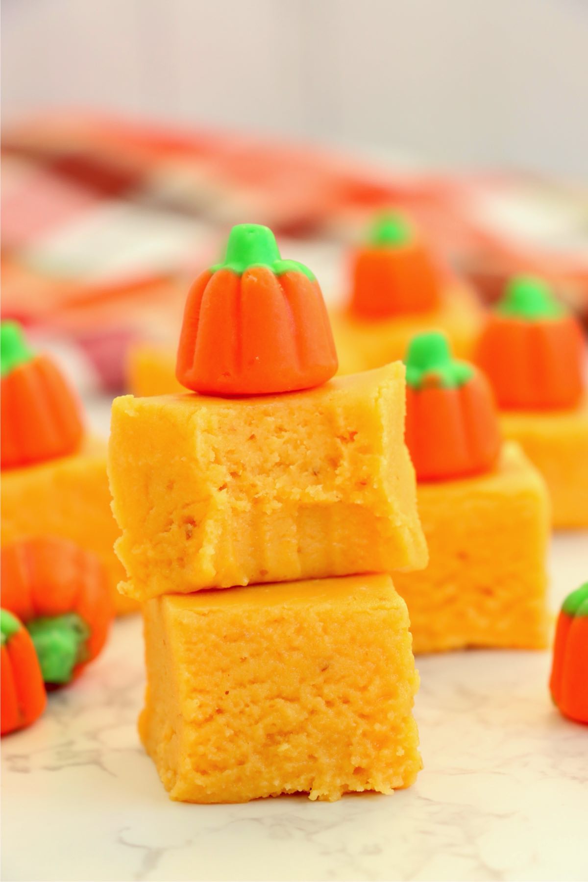 Close-up of two stacked pumpkin fudge squares topped with a candy pumpkin, with a bite taken from the top piece.