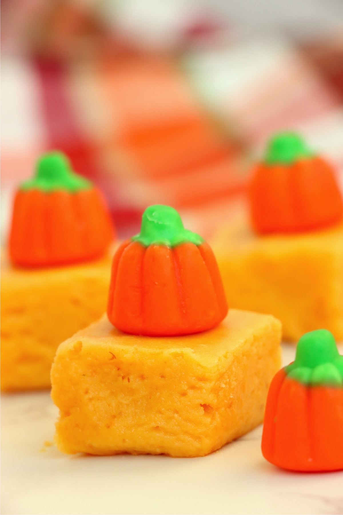 Pumpkin fudge squares topped with candy pumpkins arranged on a light surface with fall colors in the background.