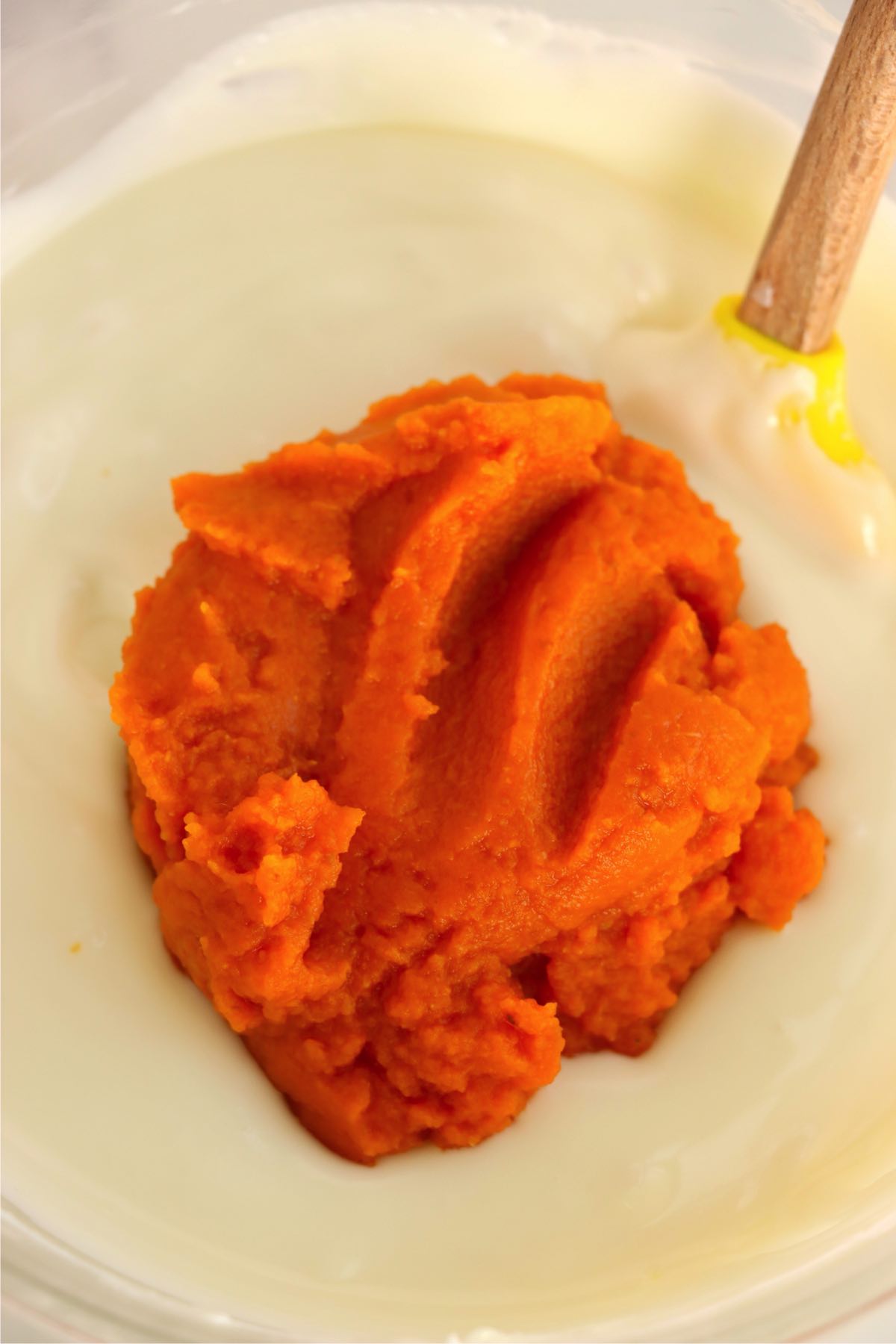 Pumpkin puree added to a bowl of smooth melted white chocolate before mixing.