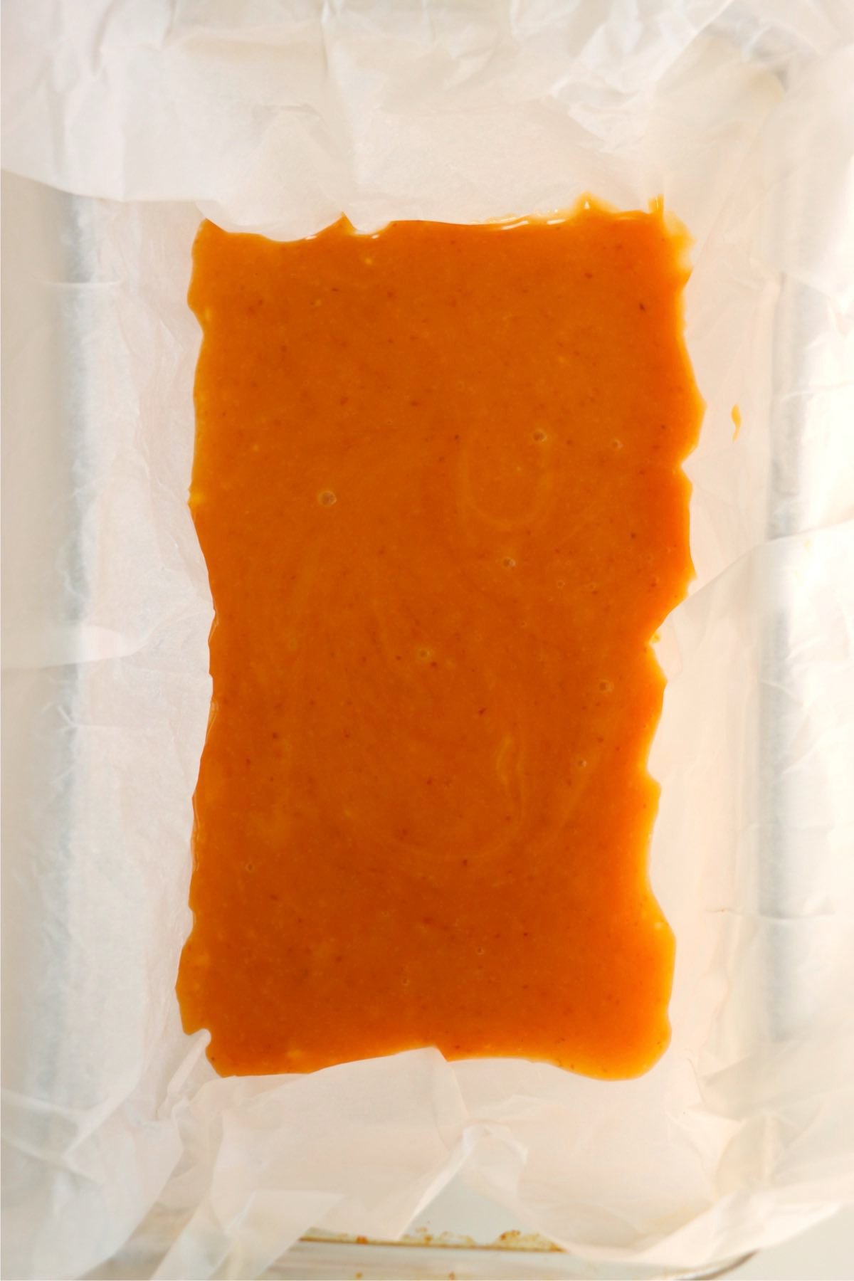Pumpkin fudge mixture poured evenly into a parchment-lined loaf pan.