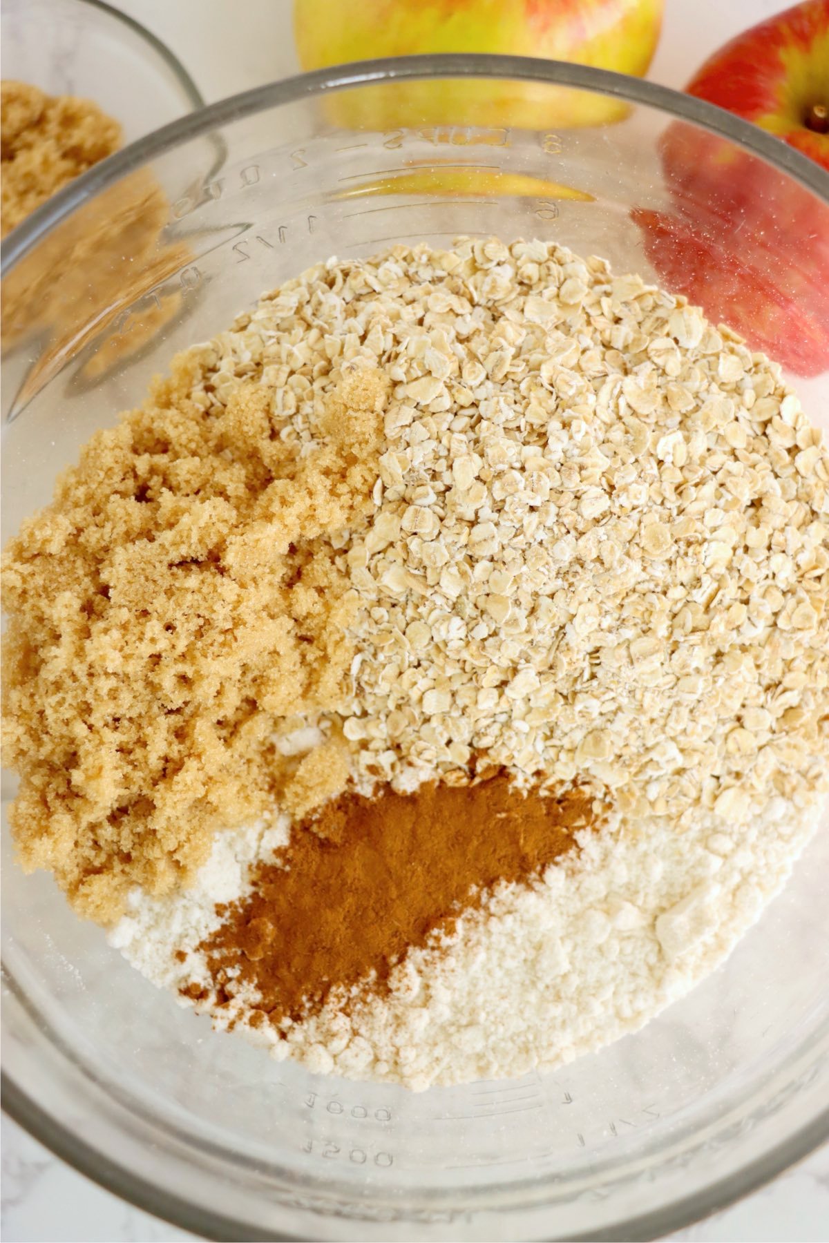 A glass bowl filled with brown sugar, rolled oats, flour, and cinnamon, ready to be mixed for a crumble topping.