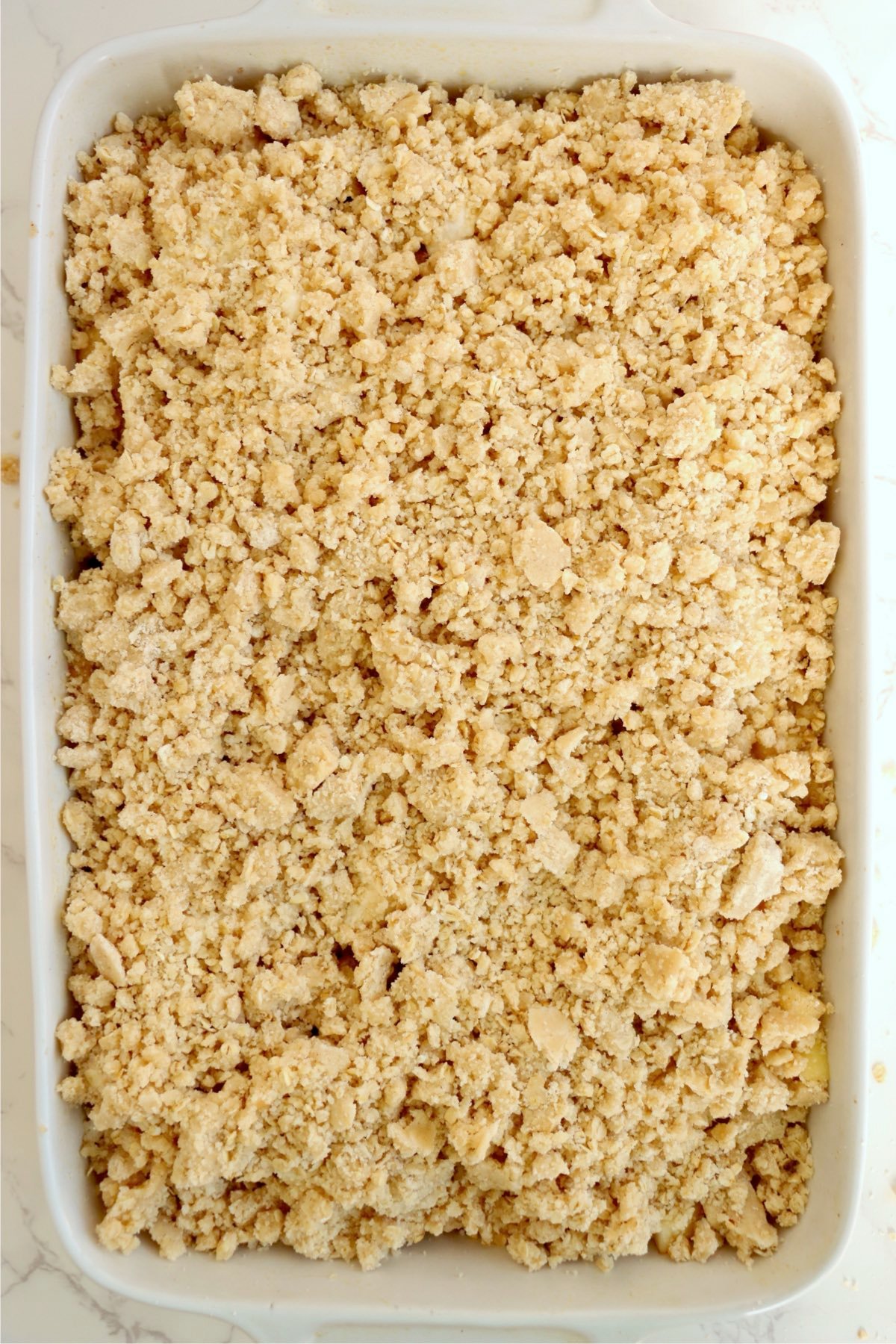 Baking dish covered with a crumbly oat topping before going into the oven.