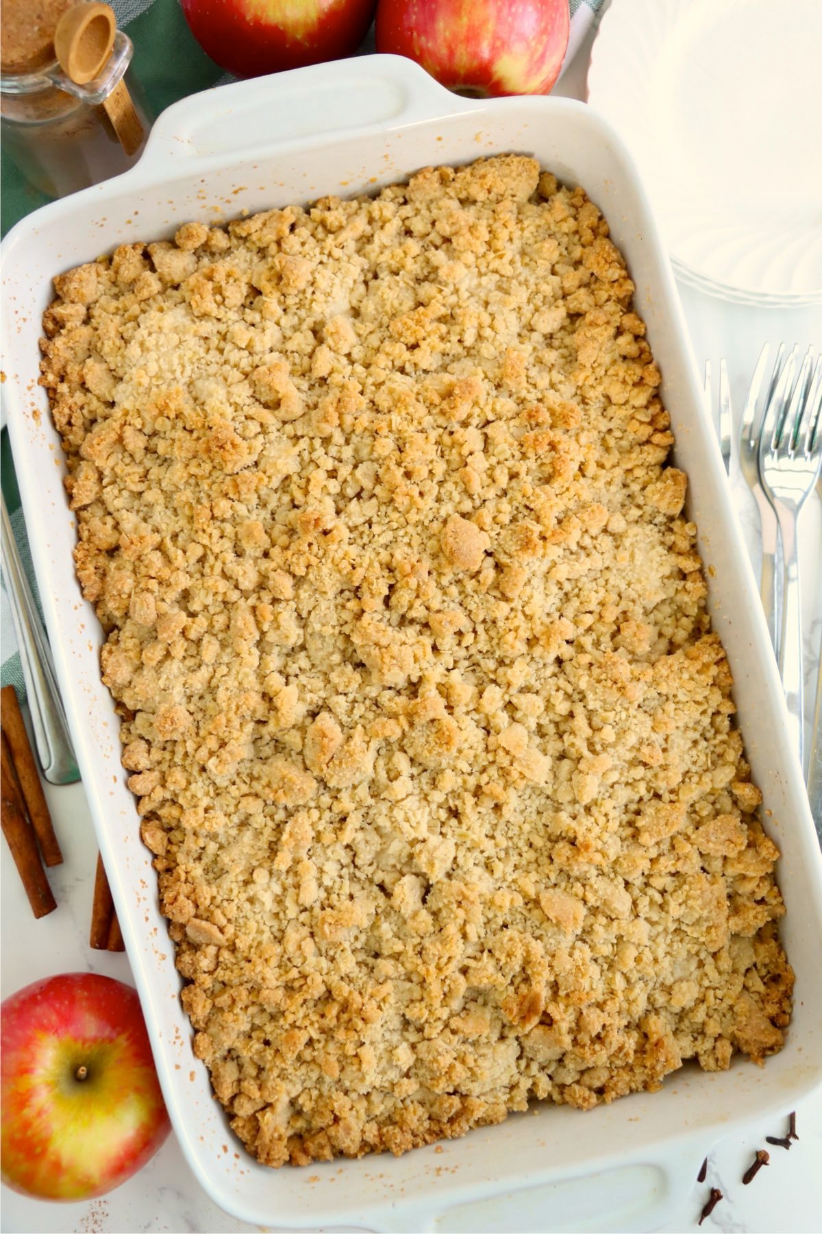Freshly baked golden crumble in a rectangular pan surrounded by apples and cinnamon sticks.
