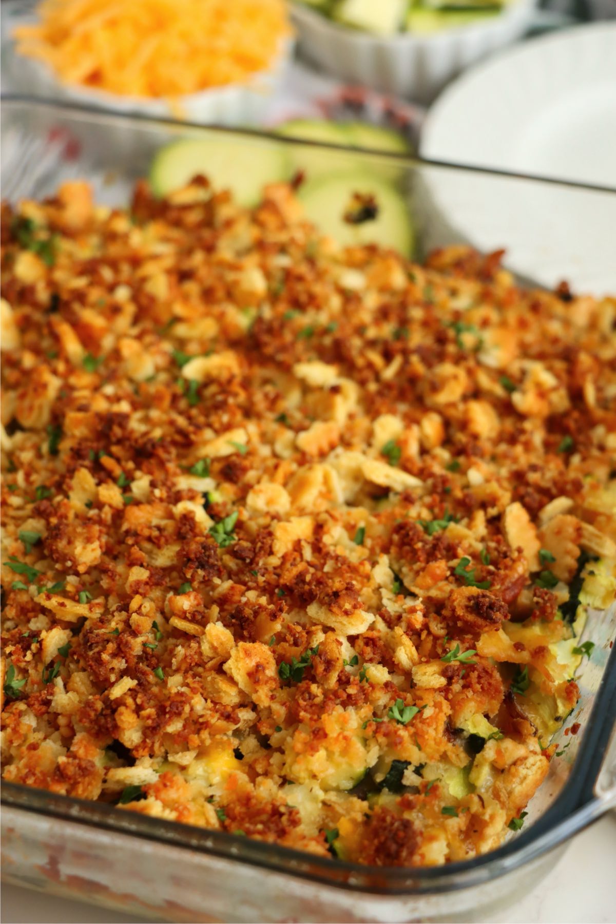 Close-up of cheesy zucchini bake in a glass dish with a golden, crispy cracker topping.