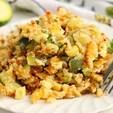 Serving of cheesy zucchini bake on a plate with a fork, featuring chunks of zucchini and melted cheese.