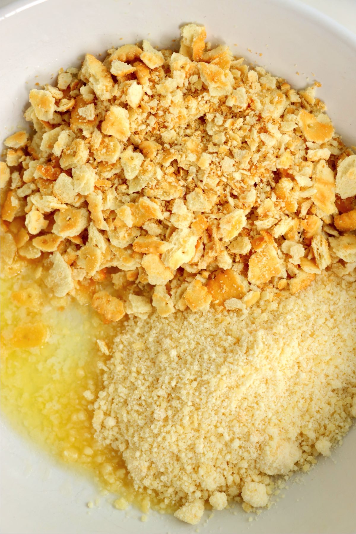 Crushed crackers, Parmesan cheese, and melted butter combined in a bowl.