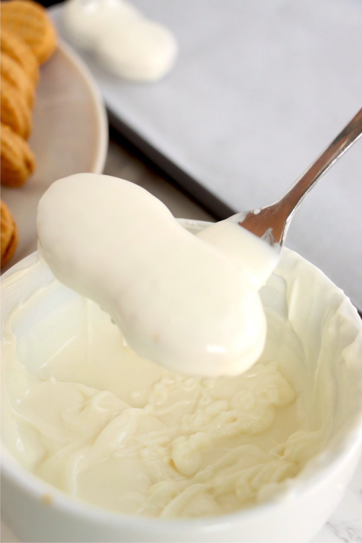 A Nutter Butter cookie coated in smooth melted white chocolate being lifted from a bowl with a spoon.