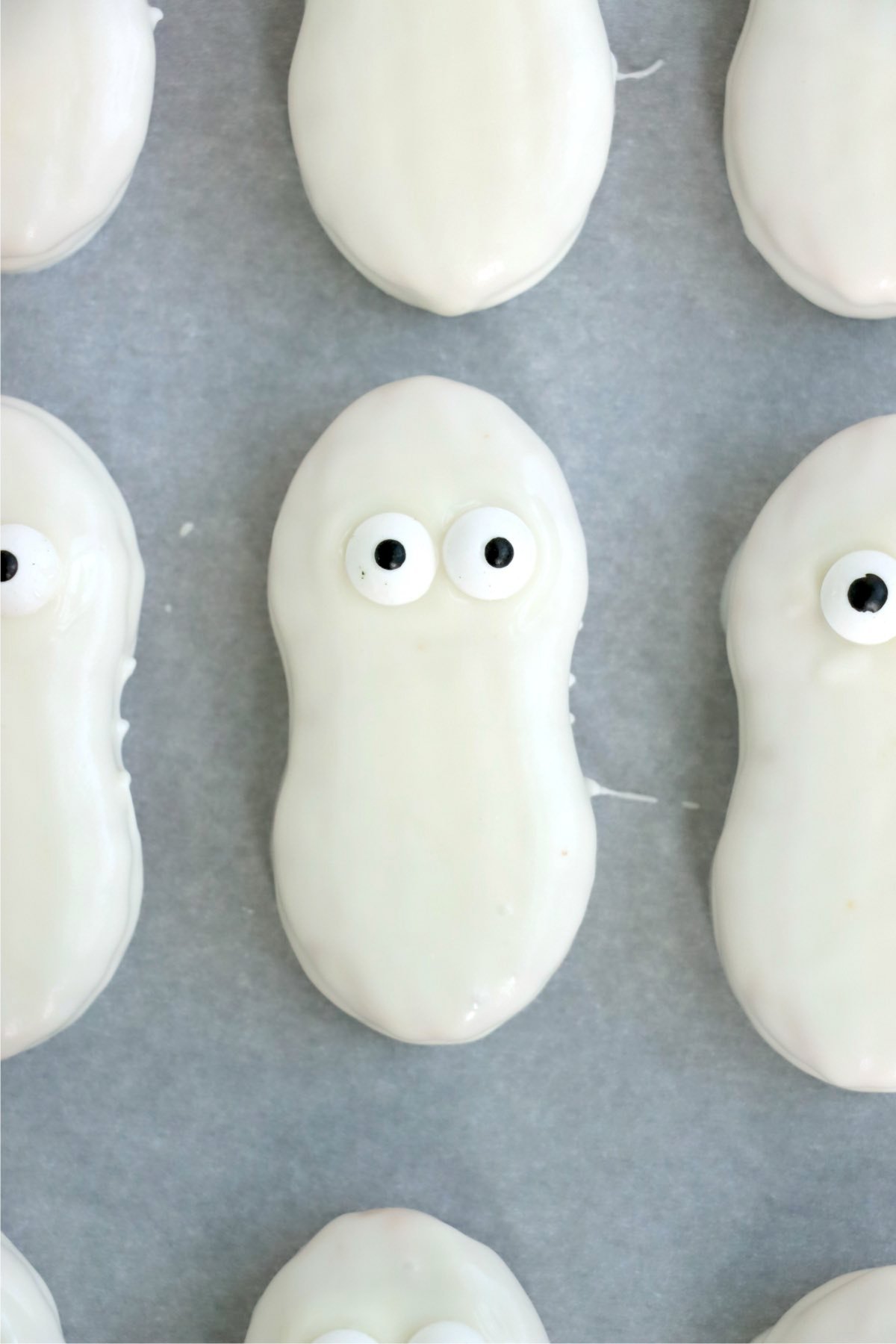A row of white-chocolate-coated cookies on parchment paper, each topped with two candy eyes.