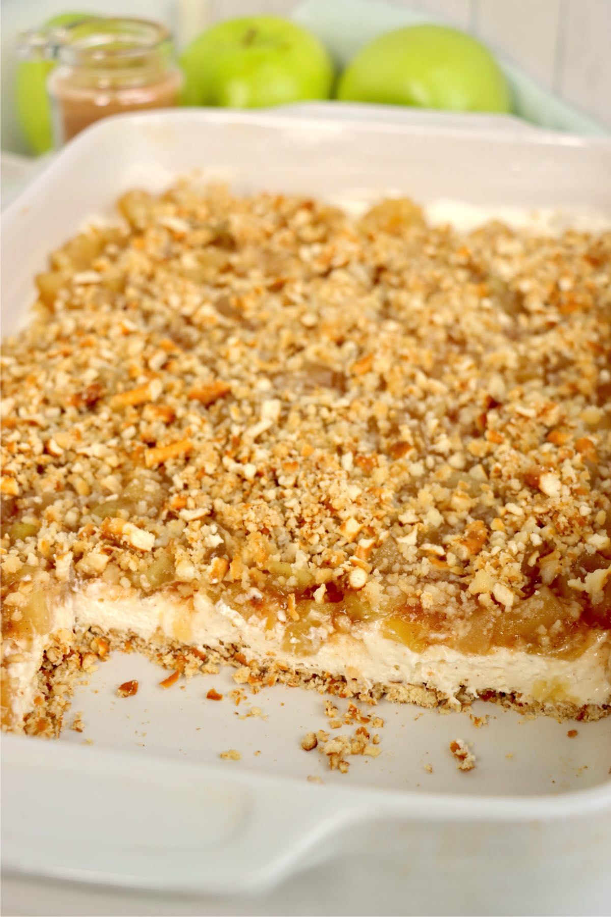 Partially sliced apple cinnamon pretzel salad in the baking dish, revealing the distinct dessert layers.