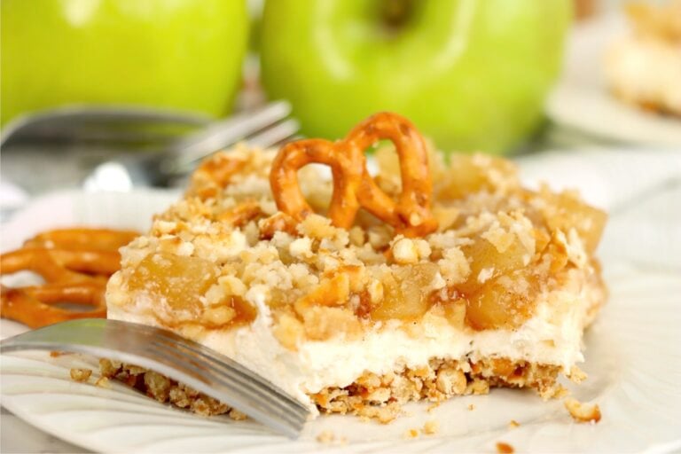 Apple cinnamon pretzel salad topped with a pretzel twist, showing the creamy filling, apple topping, and crunchy crust.