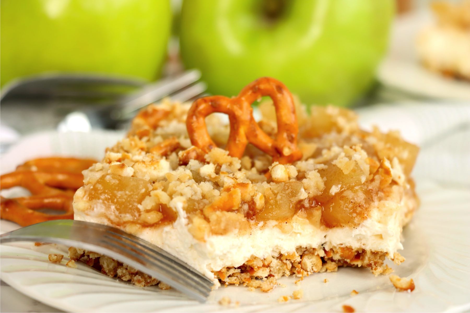 Apple cinnamon pretzel salad topped with a pretzel twist, showing the creamy filling, apple topping, and crunchy crust.