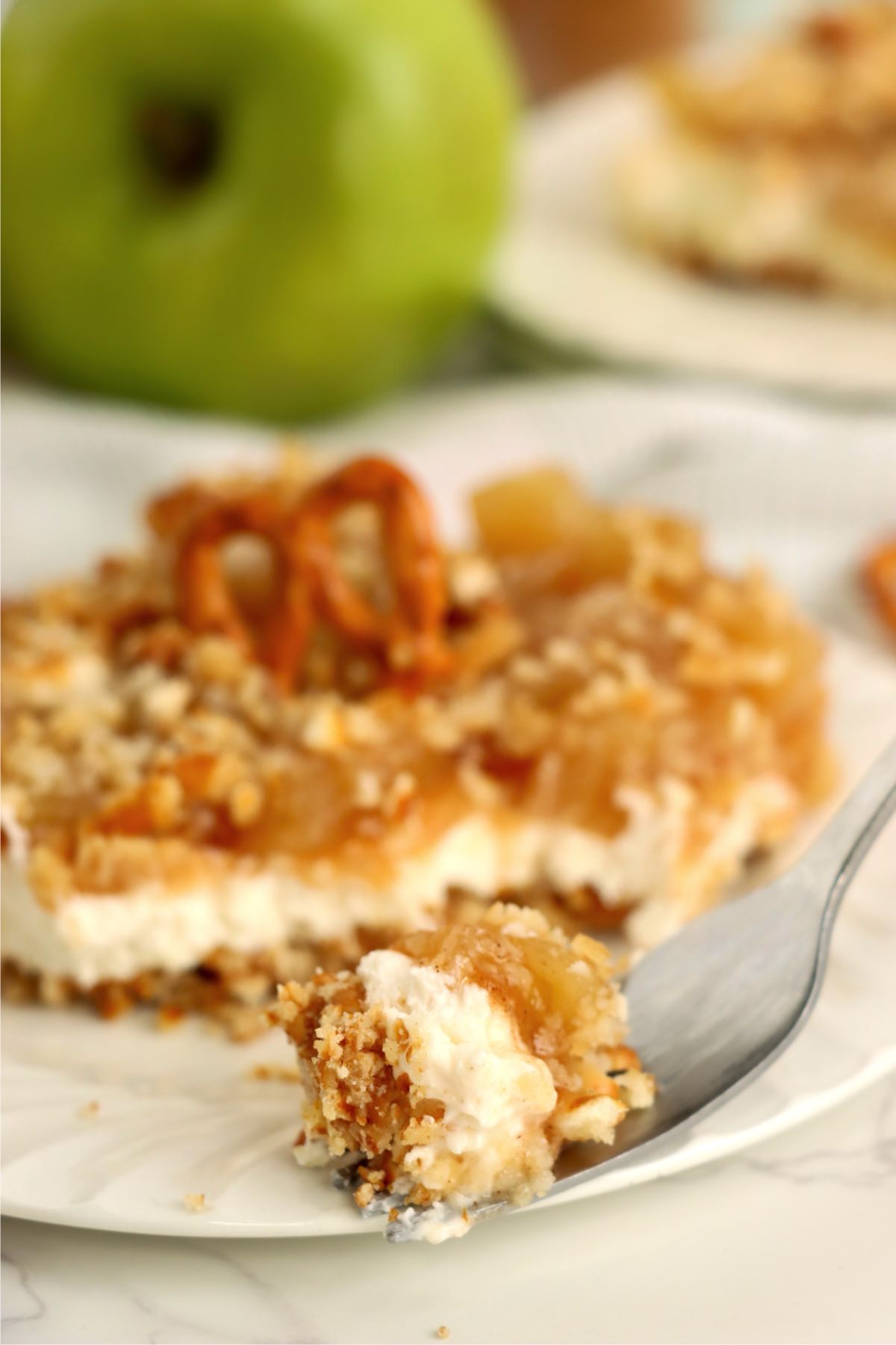 A forkful of pretzel salad lifted from the plate, highlighting the layers of pretzel crust, cream cheese filling, and cinnamon apples.