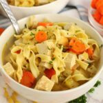Bowl of turkey soup in a white bowl with carrots and egg noodles.