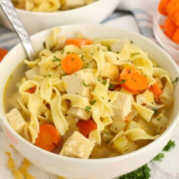 Bowl of turkey soup in a white bowl with carrots and egg noodles.