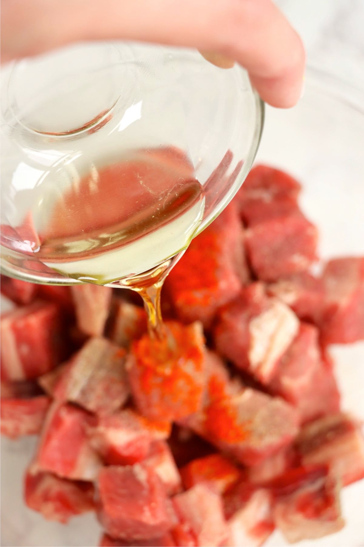 Olive oil being poured over seasoned ribeye steak bites before cooking.