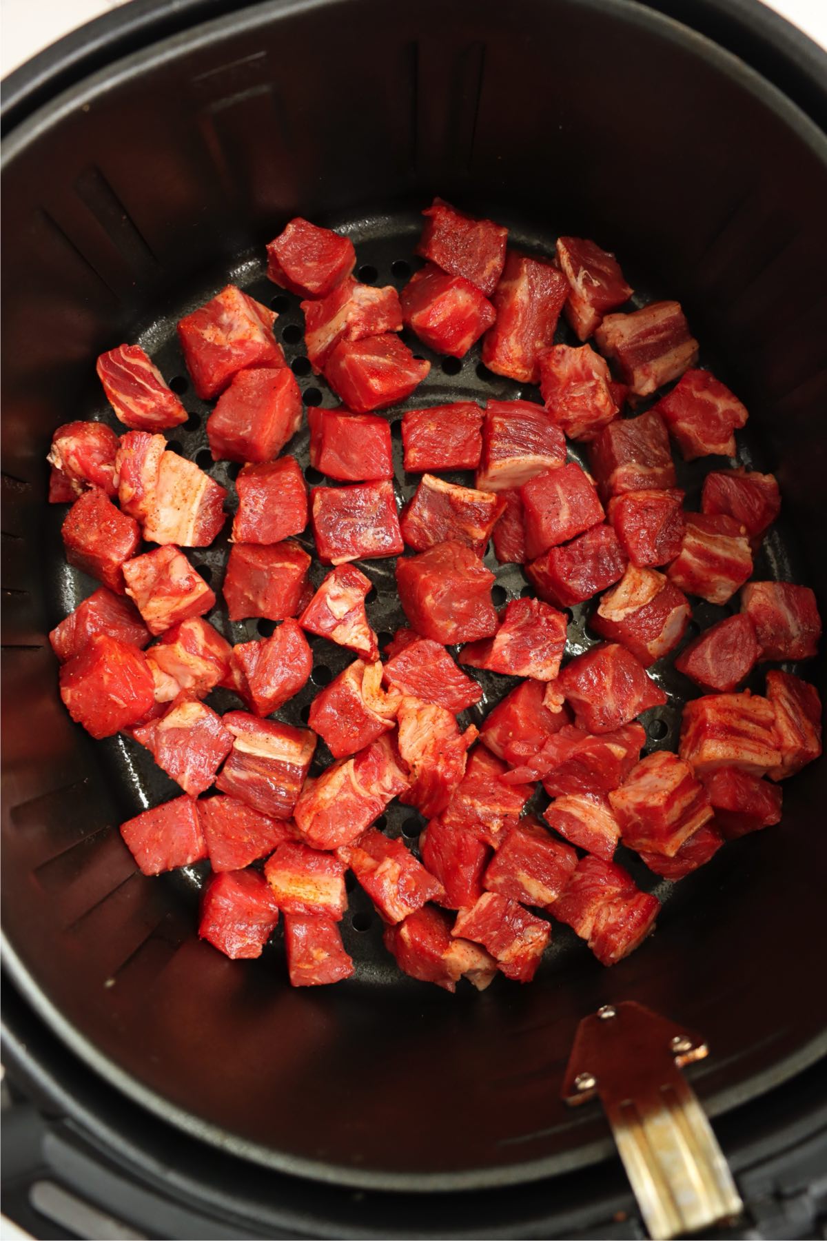 Raw steak bites arranged in a single layer in an air fryer basket.
