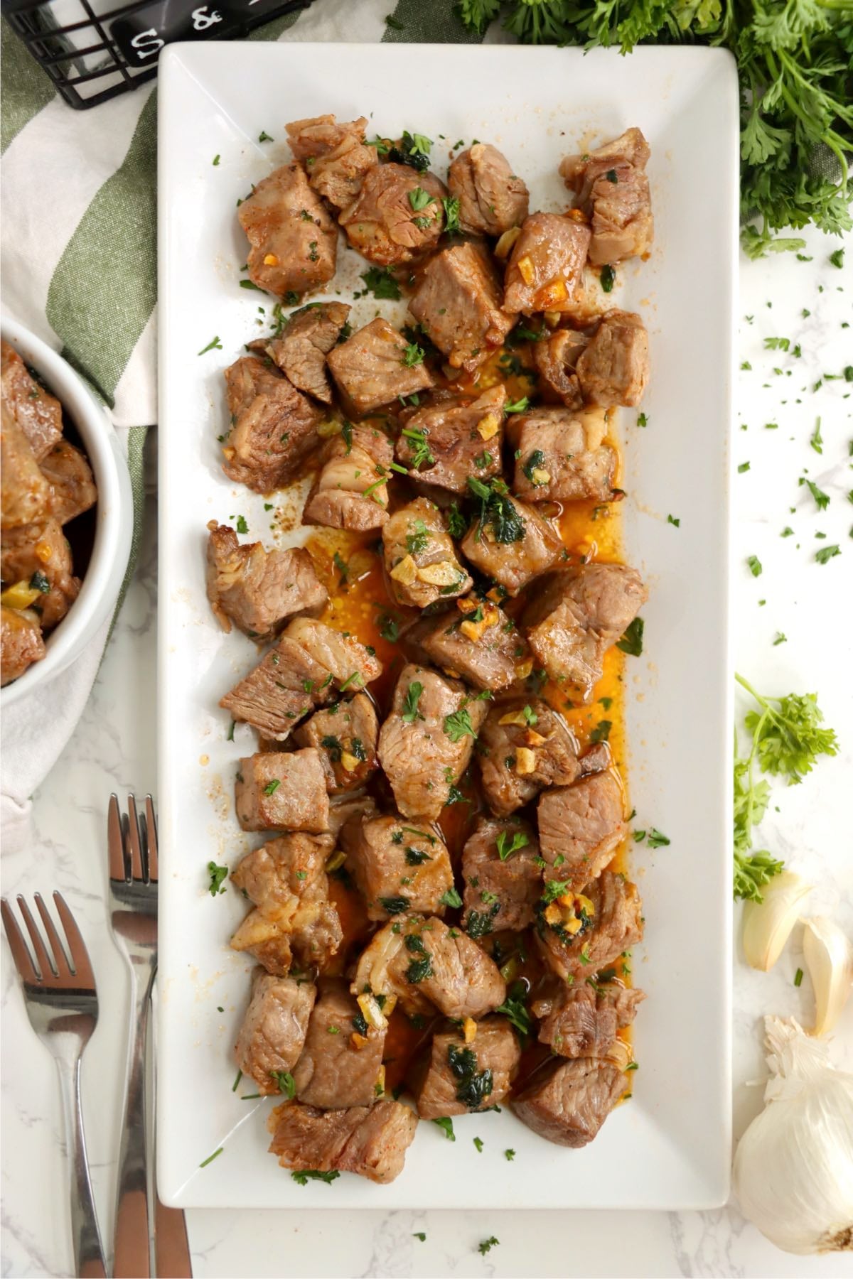 Juicy garlic butter steak bites garnished with parsley on a white tray.