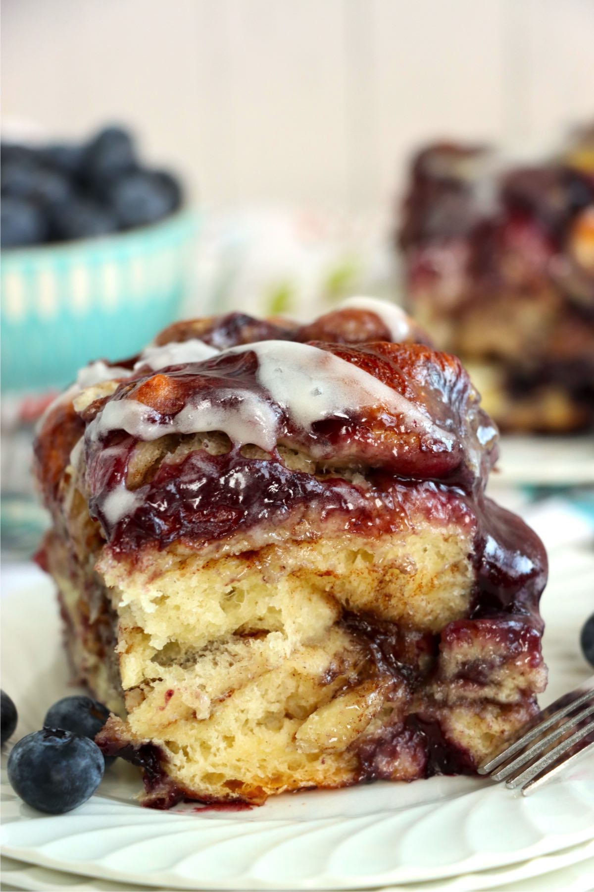 A blueberry-filled cinnamon roll with icing on a plate.