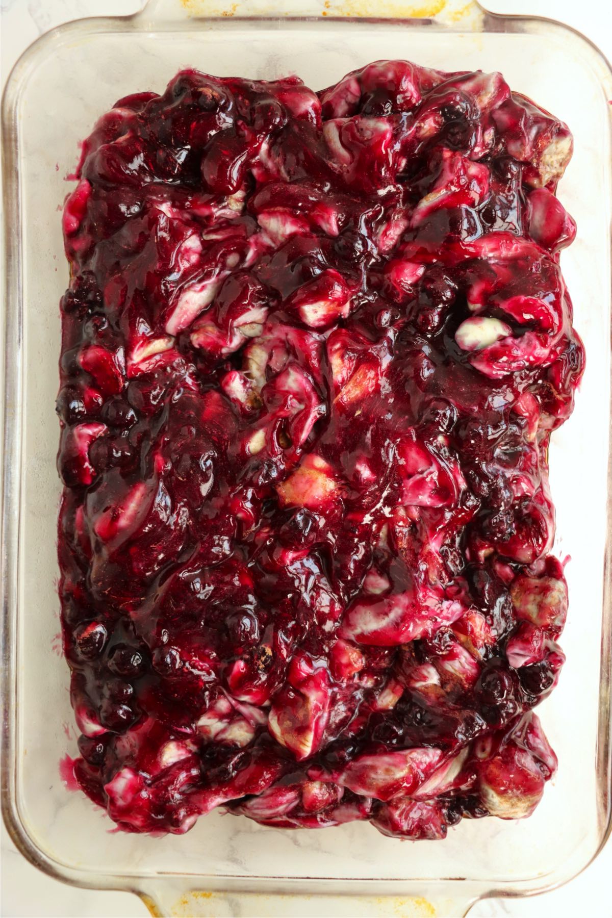 Blueberry-coated cinnamon roll mixture spread in a baking dish.