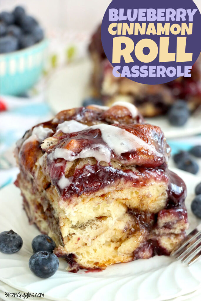 A blueberry-filled cinnamon roll topped with icing on a white plate.