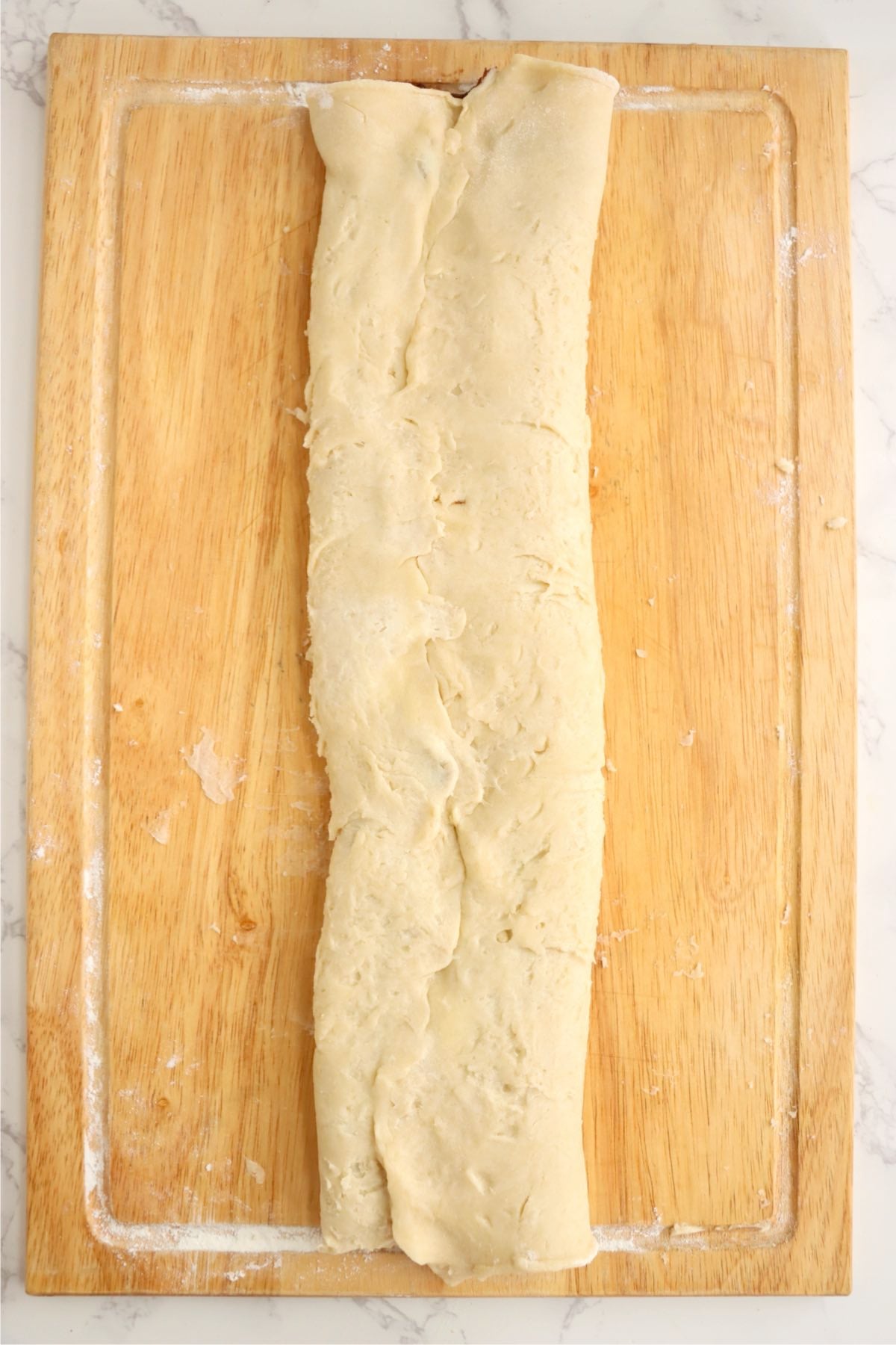 Pastry dough rolled into a long log on a wooden board.