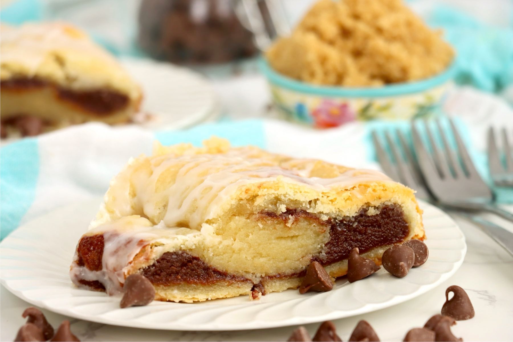 Chocolate kringle slice on a plate with chocolate chips in the foreground.
