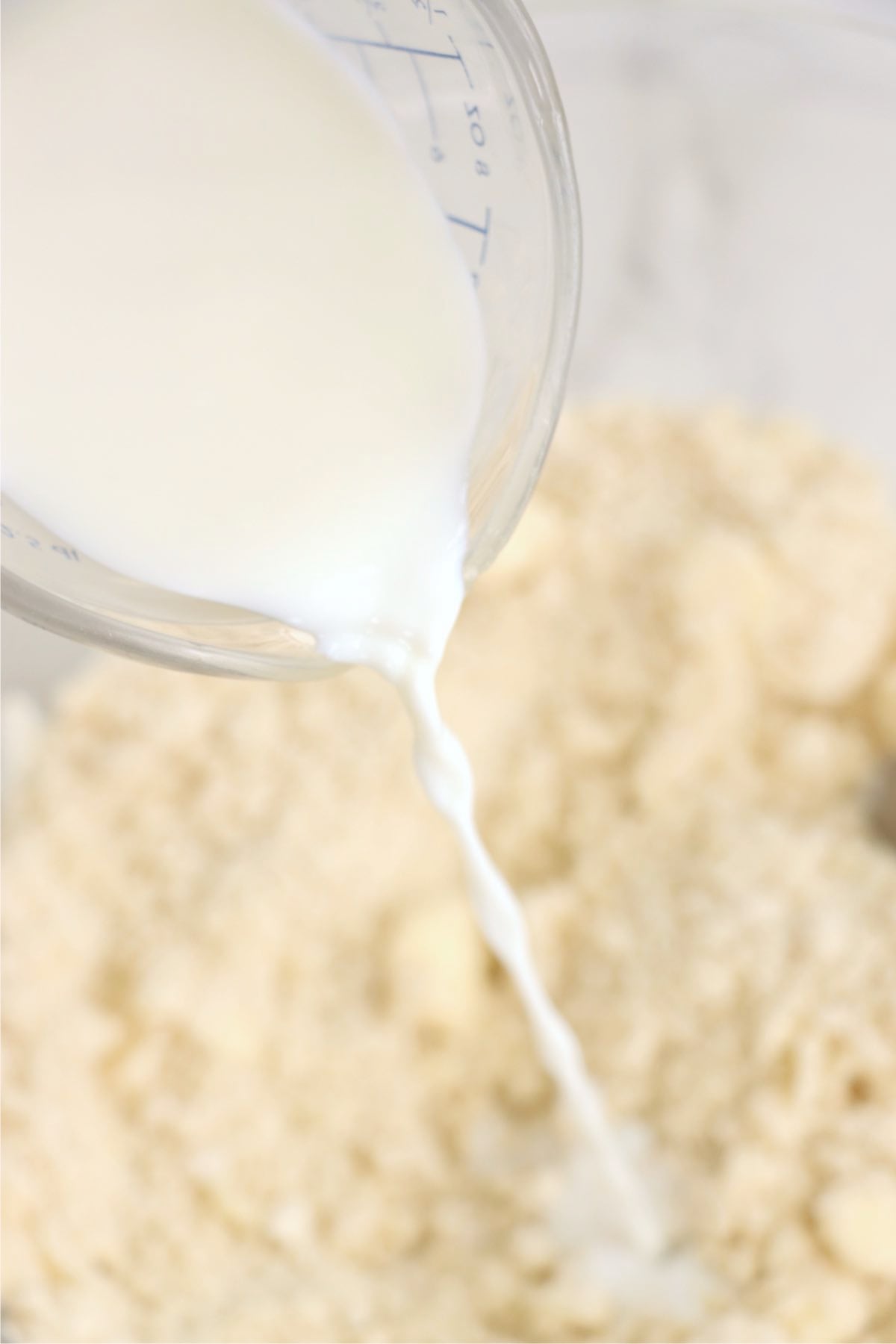 Milk being poured into a bowl of flour and butter to form a dough.