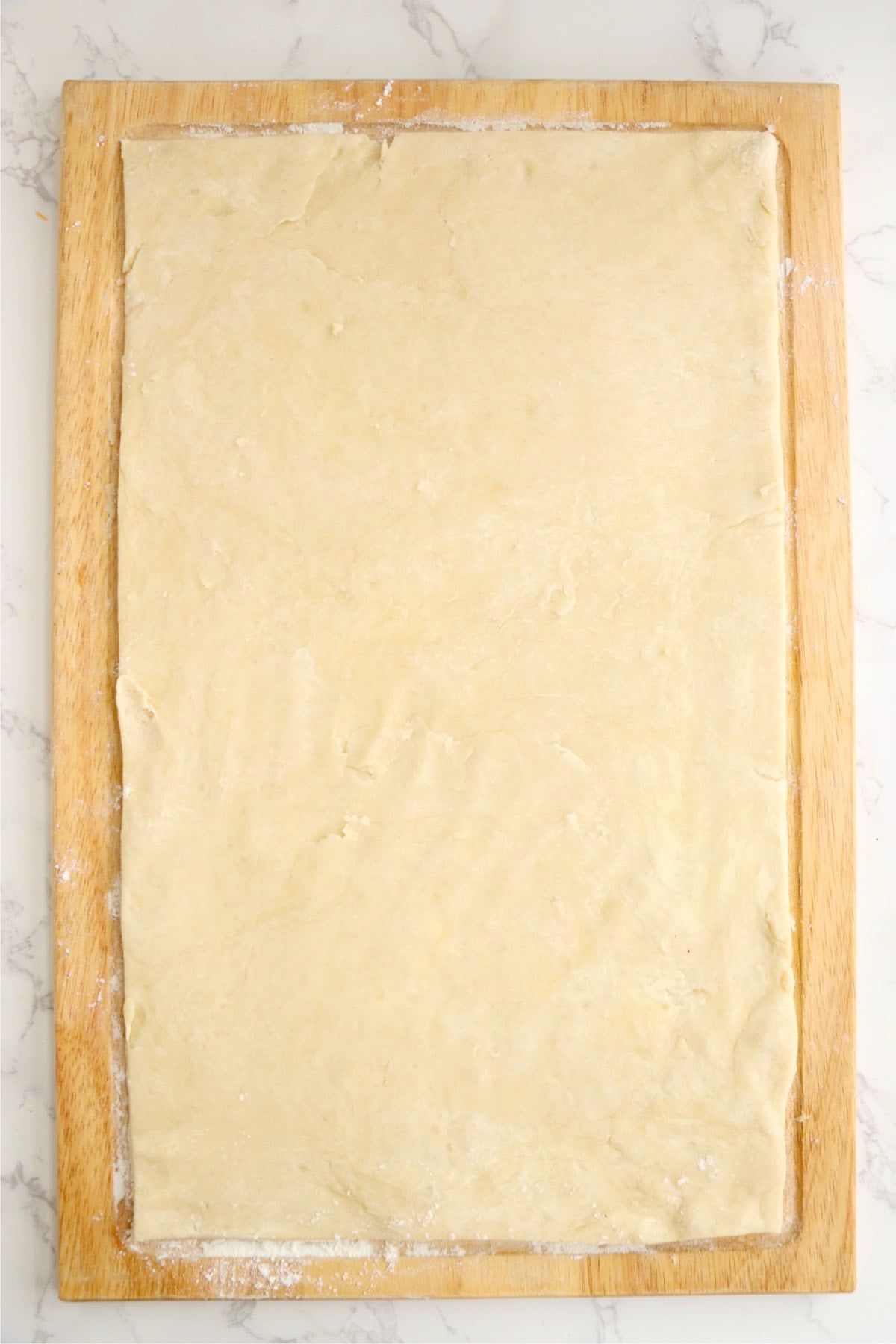 Pastry dough rolled into a large rectangle on a wooden board.