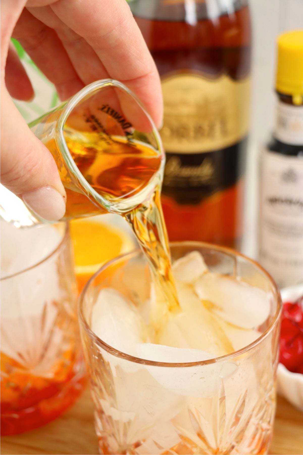 Brandy being poured into an ice-filled Old Fashioned glass during cocktail preparation.