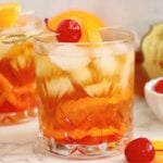 Two Wisconsin Old Fashioned cocktails garnished with orange slices and cherries on a light countertop.