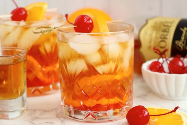 Two Wisconsin Old Fashioned cocktails garnished with orange slices and cherries on a light countertop.