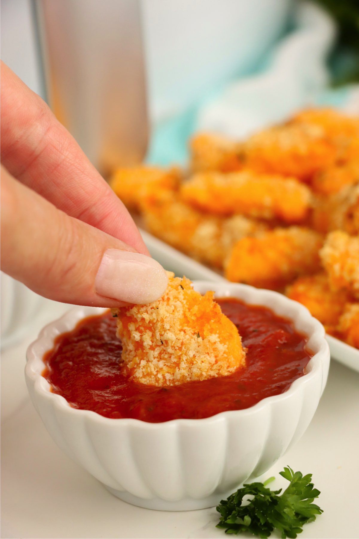 Breaded cheese curd being dipped into marinara sauce.