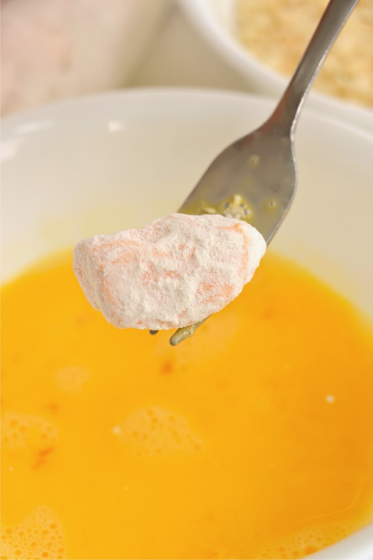 Floured cheese curd being dipped into beaten eggs.