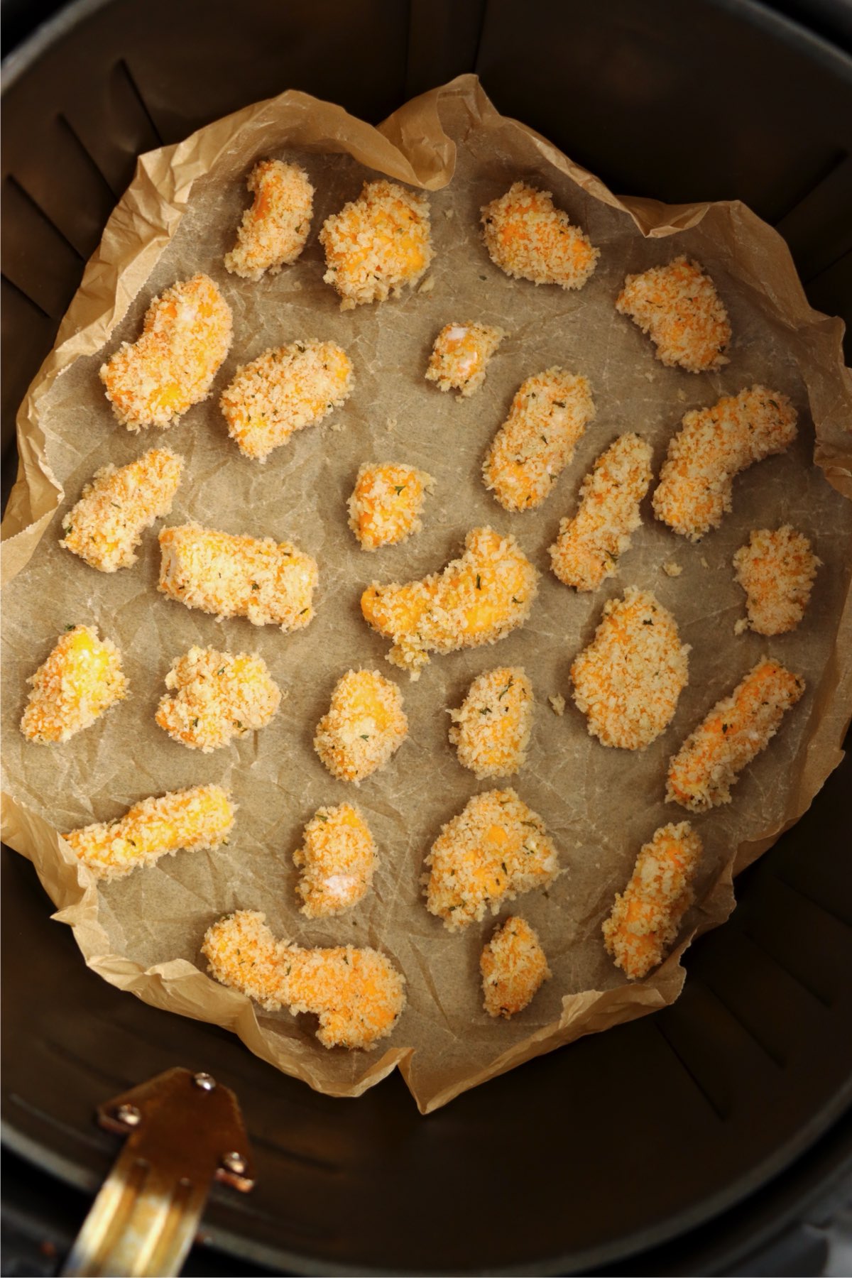 Uncooked breaded cheese curds placed in an air fryer basket.