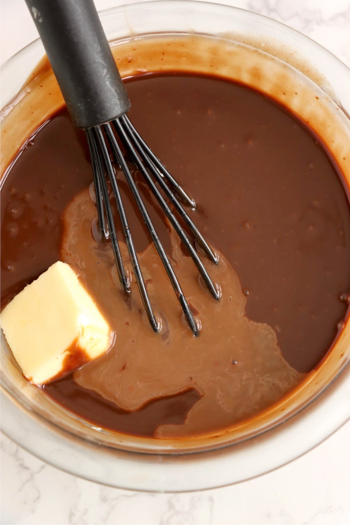 Chocolate ganache being whisked smooth with butter in a glass bowl.