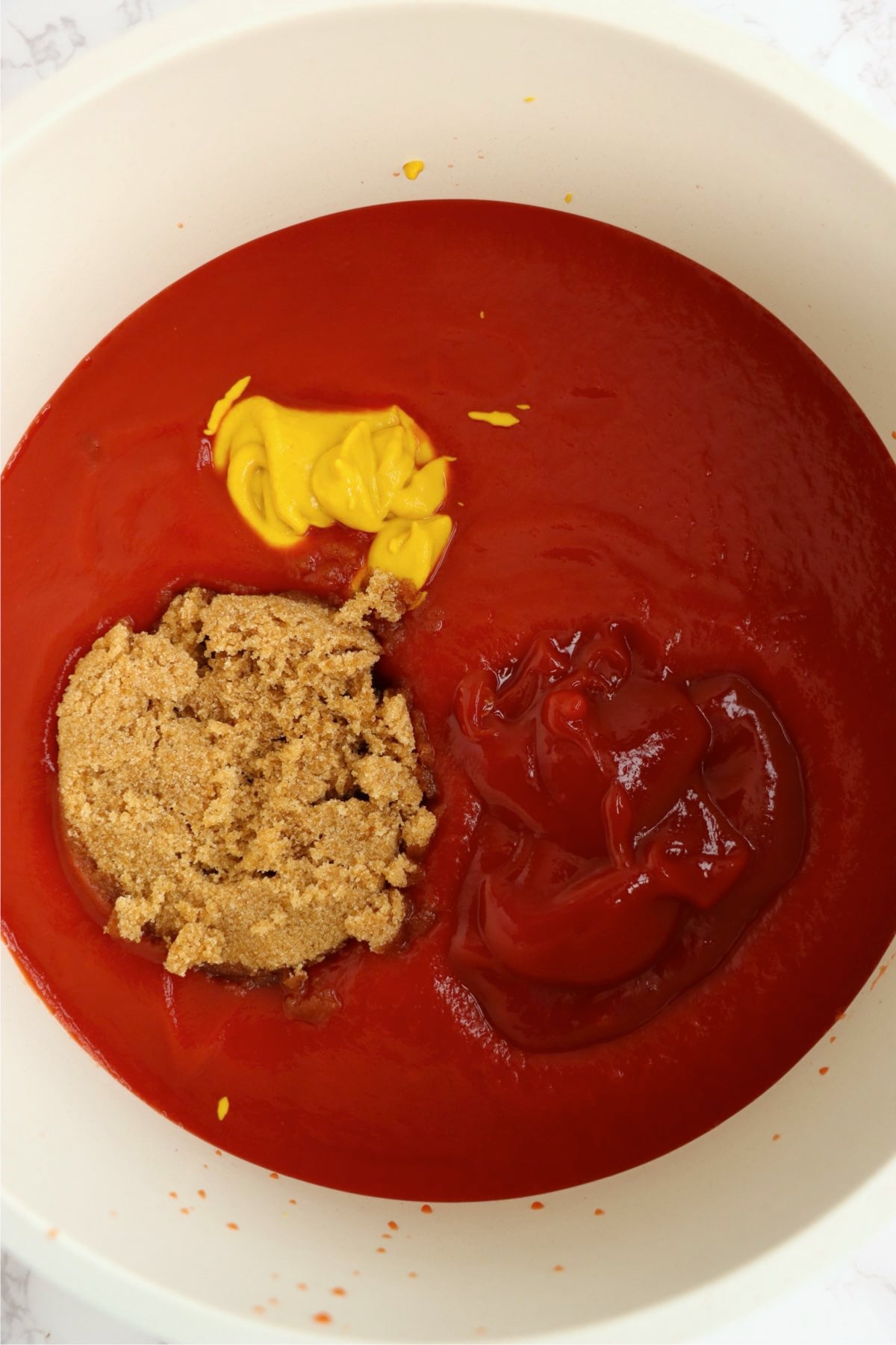 Tomato sauce, ketchup, brown sugar, and yellow mustard combined in a bowl.