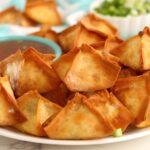 Crispy air fryer crab rangoons arranged around a bowl of dipping sauce.